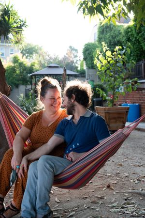 Loving couple looking at each other sitting in hammock outside in garden