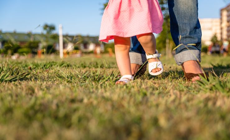 Baby girl learning to walk over a grass park