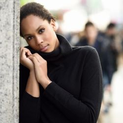Square portrait of serious woman holding neck of her dark sweater outside