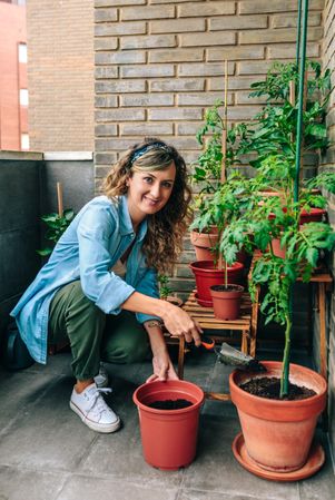 Portrait of woman using shovel to fill with soil a pot of plant in urban garden on terrace