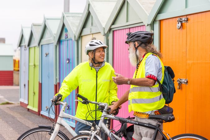 Two older people with bicycles chatting in front of colorful sheds