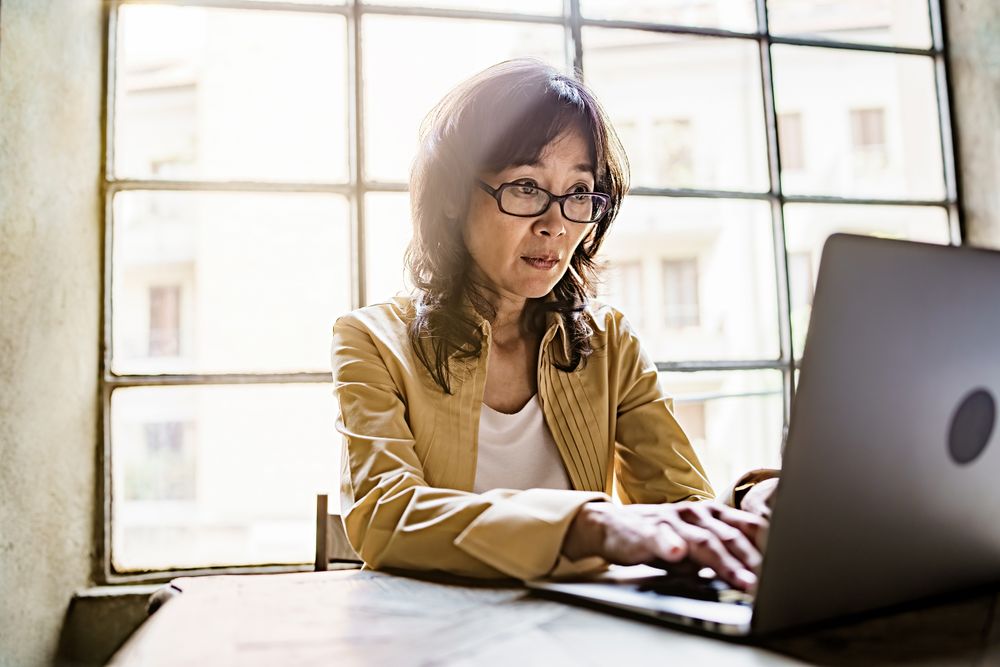 Japanese businesswoman typing on her laptop sitting in the office desk against a big window
