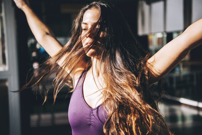 Young brunette with long waving hair moving while dancing in sunlight.