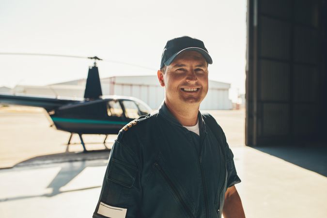Smiling helicopter pilot in cap inside hangar