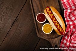 Top view of hot dog with mustard on wooden board with checkered dish towel and space for text 0yWL14