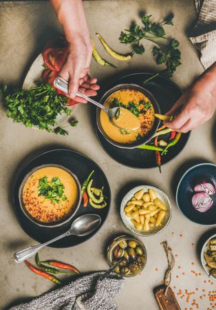 Spread of yellow lentil soup bowls, vegetable garnishes with man with spoon in soup