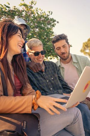 Diverse group of students collaborating with a laptop outdoors on a park bench.