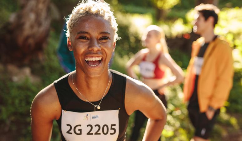 Cheerful cross country marathon runner standing outdoors looking at camera and smiling