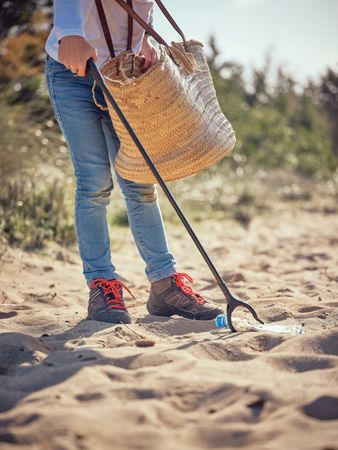 Crop person with trash grabber picking up plastic bottle