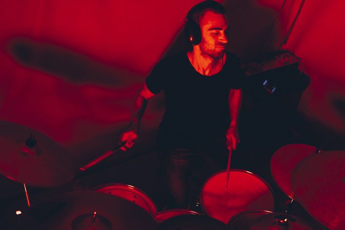 Man with drumsticks playing on drums in redness