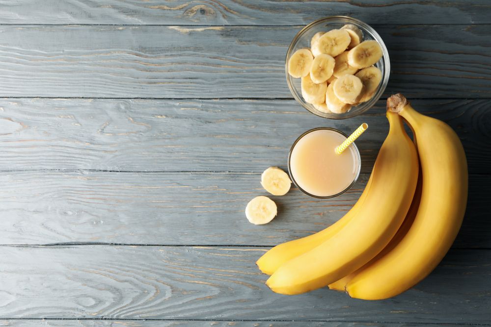 Bananas and juice on wooden background, top view