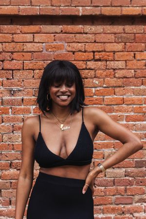 Cheerful Black woman in black outfit against brick wall