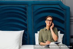 Woman sitting on a bed with a blue headboard taking a phone call 0KL1N5
