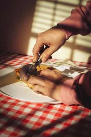 Pizza with basil being cut with knife and fork on a plate at table