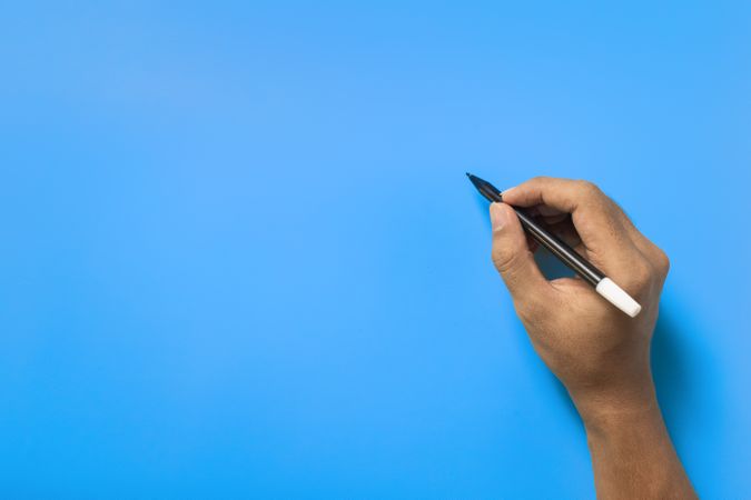 top view of male hand writing on blue blank surface
