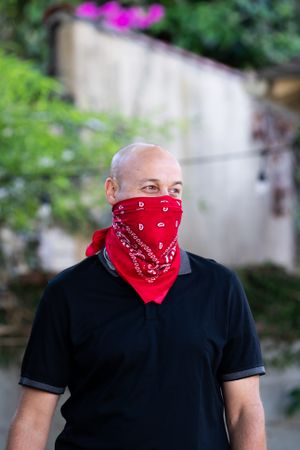 Man wearing a red bandana as PPE for coronanvirus smiling and looking away