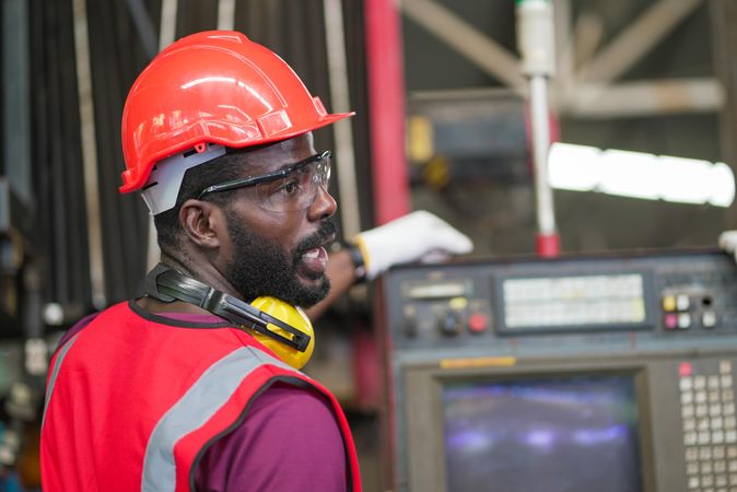 Black male factory worker operating control big machine in the industrial construction