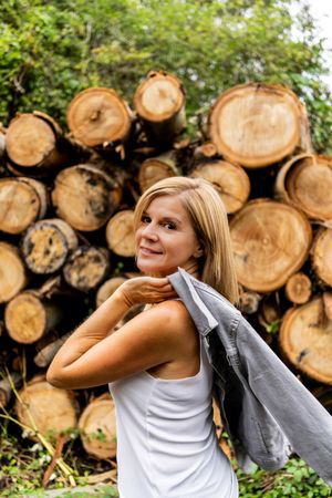 Woman taking off jacket on background of woodpile in forest