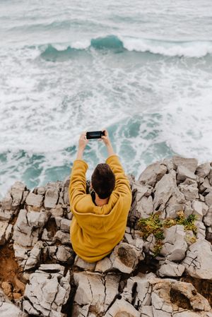 Woman in yellow hoodie taking selfie on smartphone on rocky shore