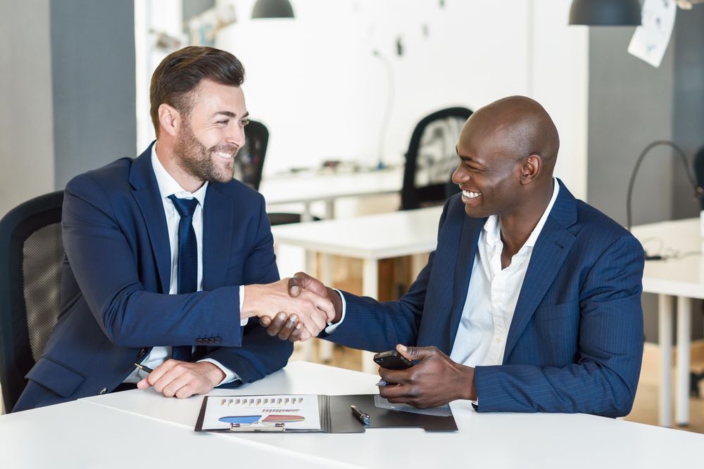 Two men wearing blue suits shaking hands in a bright office