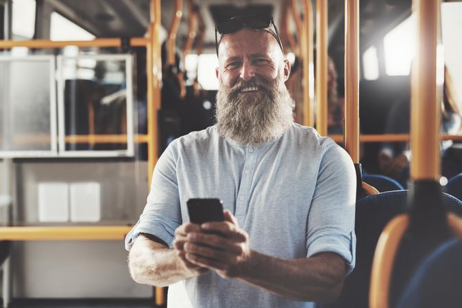 Man with gray beard smiling with phone on public transport