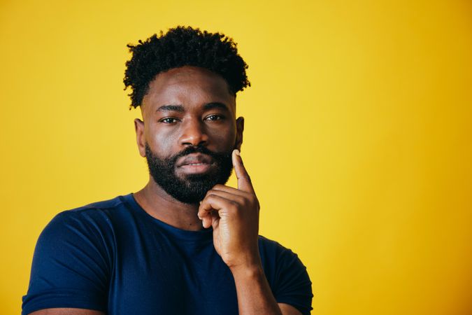 Portrait of curious Black man with hand to his temple on yellow background