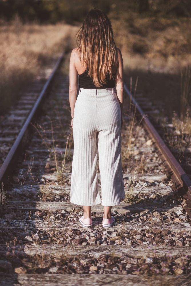 Long haired woman standing on railways overgrown with dry grass