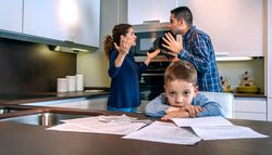 Couple arguing in front of little boy with bills strewn on the kitchen counter