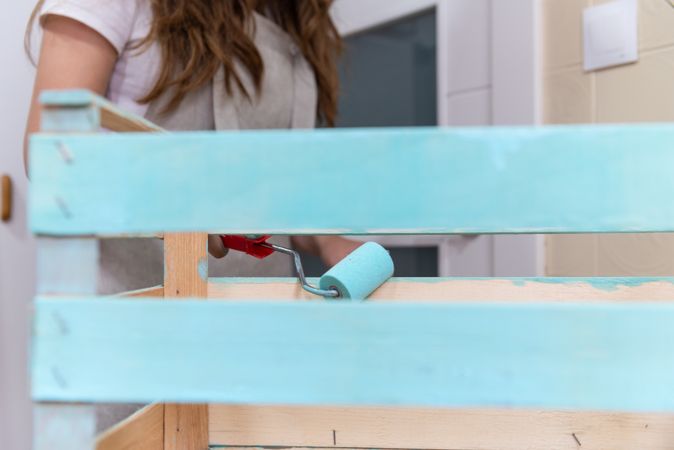 Woman paining wooden box in blue color with roller