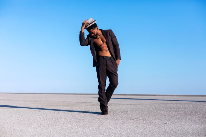 Black man holding his hat while dancing against blue sky on a sunny day