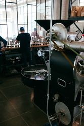 Master roaster tasting coffee with roasting machine in foreground