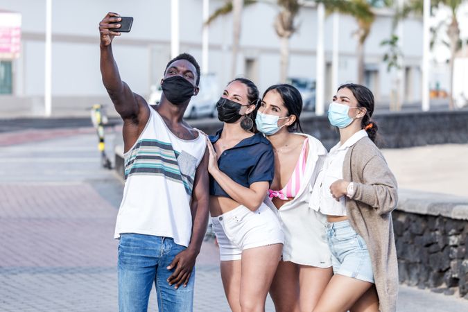 Group of women and man wearing face masks and taking selfie
