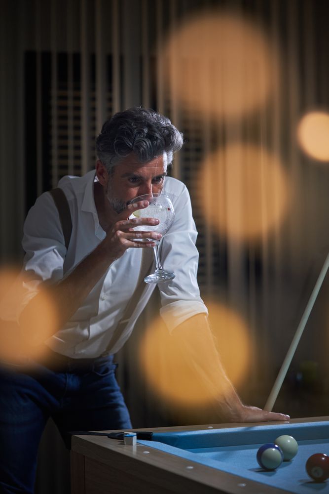 Mature male standing at pool table and drinking cocktail
