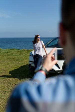 Guy taking picture of woman leaning on a car