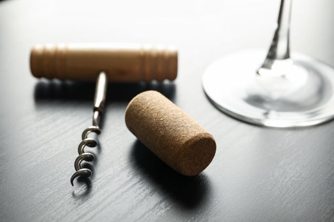 Corkscrew, cork and wine glass on dark table, close up