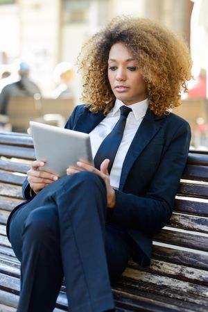 Woman in suit using her digital tablet on outdoor bench