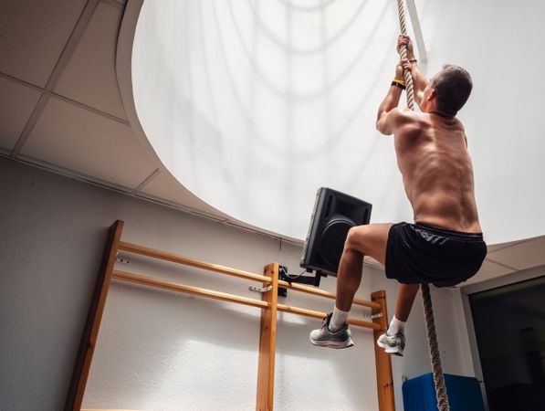 Muscular athlete climbing rope in gym