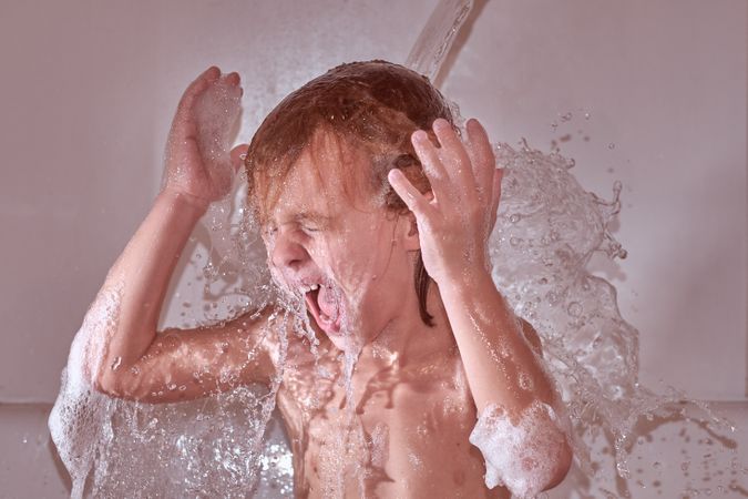 Boy under pouring water in bathtub