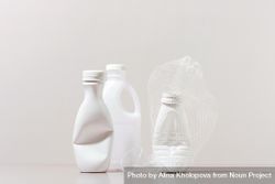 Three crushed plastic bottles and cup on neutral background 4MwGx0