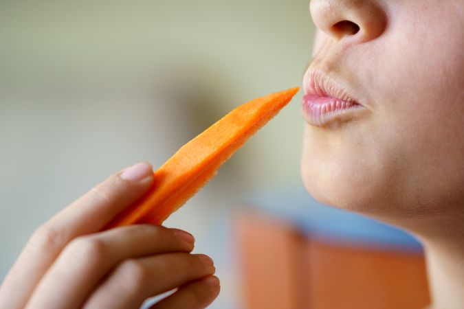 Anonymous girl puckering lips while holding fresh carrot slice