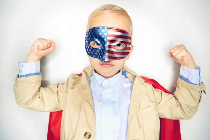Serious blond boy wearing American flag mask making muscles