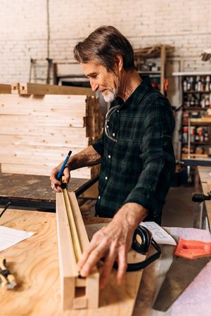 Mature male carpenter extending measuring tape on wooden block, vertical