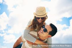 Woman piggy backing on boyfriend’s back against a blue sky with clouds 4OlmRb