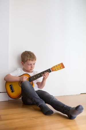Young blonde boy playing toy guitar