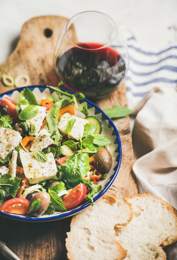 Greek salad with feta, tomatoes, and red wine on wooden board, vertical composition, selective focus