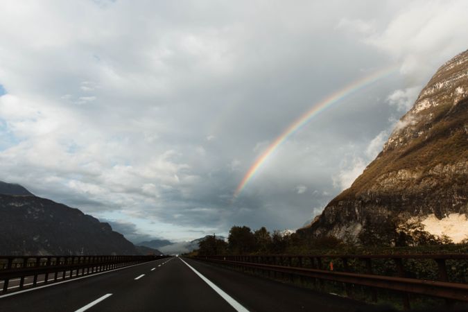 Lonely highway amid mountains and sky with rainbow