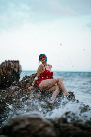Graceful woman with trendy hairstyle tanning on rocky stone in water