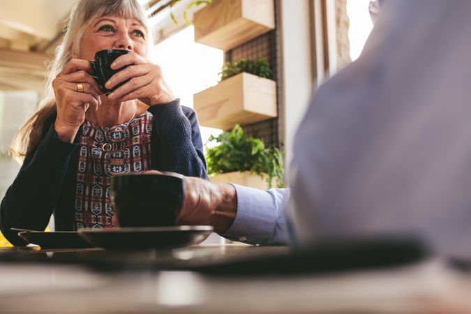 Mature woman sitting at cafe drinking a cup of coffee and talking with her husband