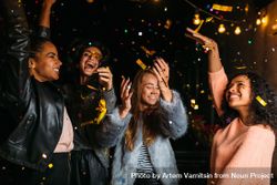 Multi-ethnic group of stylish women throwing confetti at night 0vrn70