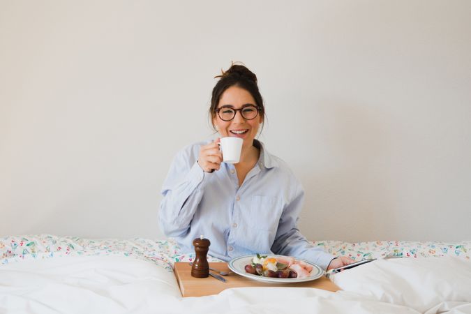 Young woman with breakfast on bed using smart phone